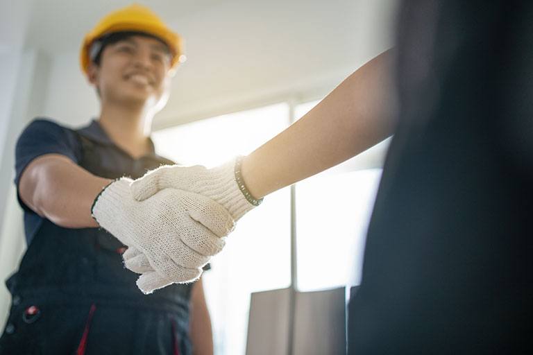 Close-up of a handshake between a contractor wearing work gloves and a client, symbolizing trust, agreement, and customer satisfaction in a well-lit construction environment.