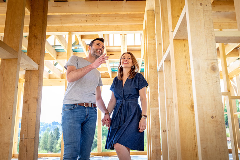 Happy couple touring a new home under construction, surrounded by wooden framing.